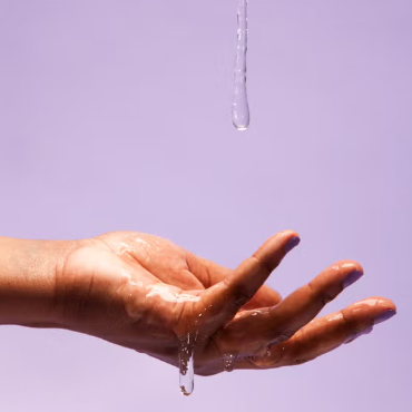 Hand catching a drop of lubricant against a lavender background